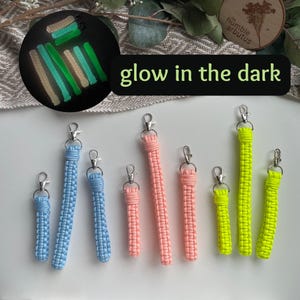 May include: A set of eight glow-in-the-dark keychains in various colours, including blue, pink, and yellow. The keychains are made of braided cord and have silver metal clasps. The image includes the text "glow in the dark".