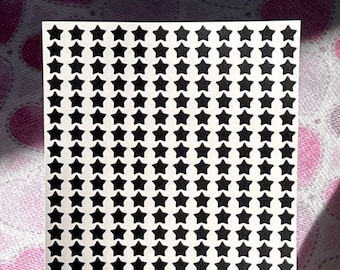 May include: A sheet of white paper with a grid of black star stickers. The stars are evenly spaced and arranged in rows and columns.