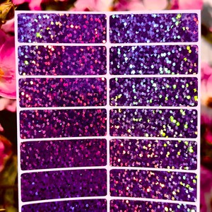 May include: A sheet of twelve rectangular stickers featuring a deep purple base colour with a dense, multi-coloured holographic glitter finish. The stickers are arranged in two vertical columns of six, each with rounded corners and a white border.