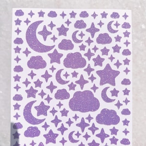 May include: A sheet of purple glitter stickers featuring clouds, stars, and crescent moons.