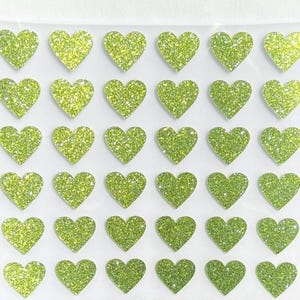 May include: Sheet of lime green glitter heart stickers. Each heart is a vibrant, sparkling green, arranged in neat rows and columns. The stickers have a glossy, textured appearance, perfect for crafts and decorations.