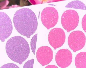 May include: A sheet of adhesive stickers featuring multiple balloon shapes in glittery purple and bright pink. The balloon stickers are arranged in a repeating pattern on a white backing, each displaying a textured, sparkling finish.