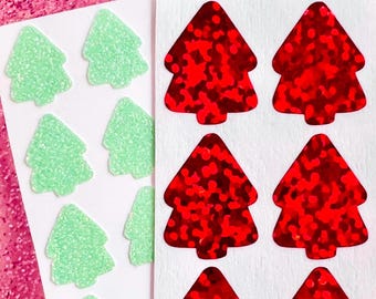 Könnte beinhalten: Ein Bogen mit Aufklebern in Form von ausgestanzten Weihnachtsbäumen. Ein Bereich enthält hellminzgrüne Glitzeraufkleber, während der andere Bereich leuchtend rote holografische Folienaufkleber mit einer reflektierenden Textur zeigt.