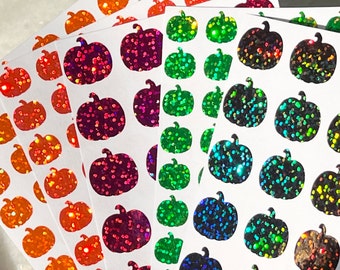 Könnte beinhalten: Bogen mit Aufklebern mit verschiedenen Farben von Glitzerkürbissen. Die Aufkleber befinden sich auf weißen Bögen und sind bereit für Bastelarbeiten oder Dekorationen.