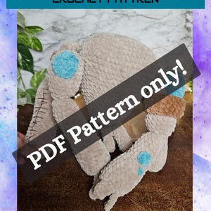 May include: A beige plush crochet alien toy with blue circular accents on its limbs and head. The toy features dark brown stitching details on one side. The image includes the text ROCKY THE ALIEN CROCHET PATTREN and PDF Pattern only!
