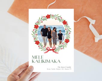 May include: A Christmas card with a watercolor wreath of green leaves, red flowers, and red berries. The wreath surrounds a photo of a family of four standing on a beach. The text "MELE KALIKIMAKA" is printed in black at the bottom of the card, along with the family's names and ages.