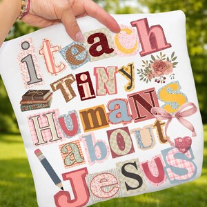 May include: White pillow with the words "I teach tiny humans about Jesus" in a patchwork style. The design includes a pencil, books, flowers, and a pink ribbon. The letters are in various colors and patterns.