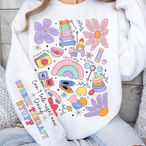 May include: White sweatshirt with a colorful graphic design featuring various toys and the text "Speech Therapy Stuff" and "Can't talk right now, Doing Speech Therapy Stuff".