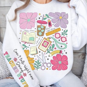 Puede incluir: Sudadera blanca con un diseño gráfico colorido que presenta flores, tazas de café, tijeras, lápices y libros. El texto en la sudadera dice "Can't talk right now Doing TEACHER STUFF".