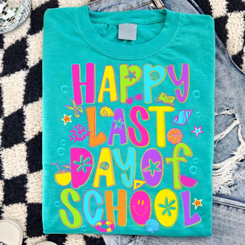 May include: Teal t-shirt with the words "HAPPY LAST DAY OF SCHOOL" in colorful, playful lettering. The design includes various summer-themed graphics like seashells, stars, and a basketball. The shirt is laid flat on a denim surface.