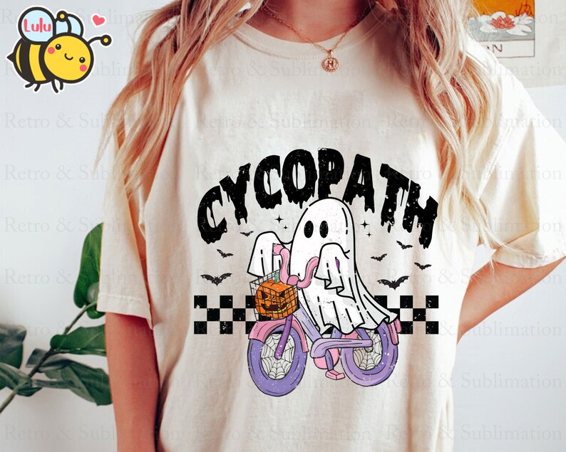 May include: A white t-shirt with a black and white graphic of a ghost riding a bicycle with a pumpkin basket. The text "CYCOPATH" is printed in black above the graphic.
