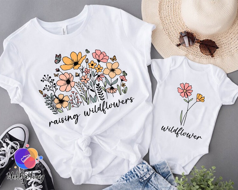 May include: White t-shirts with floral designs and the text "raising wildflowers" and "wildflower".