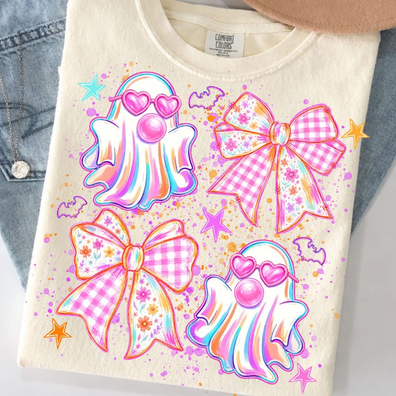May include: A cream-colored t-shirt with a graphic print featuring two ghosts wearing pink heart-shaped sunglasses and blowing bubblegum, two large bows with pink gingham and floral patterns, small purple bats, and orange and pink stars.