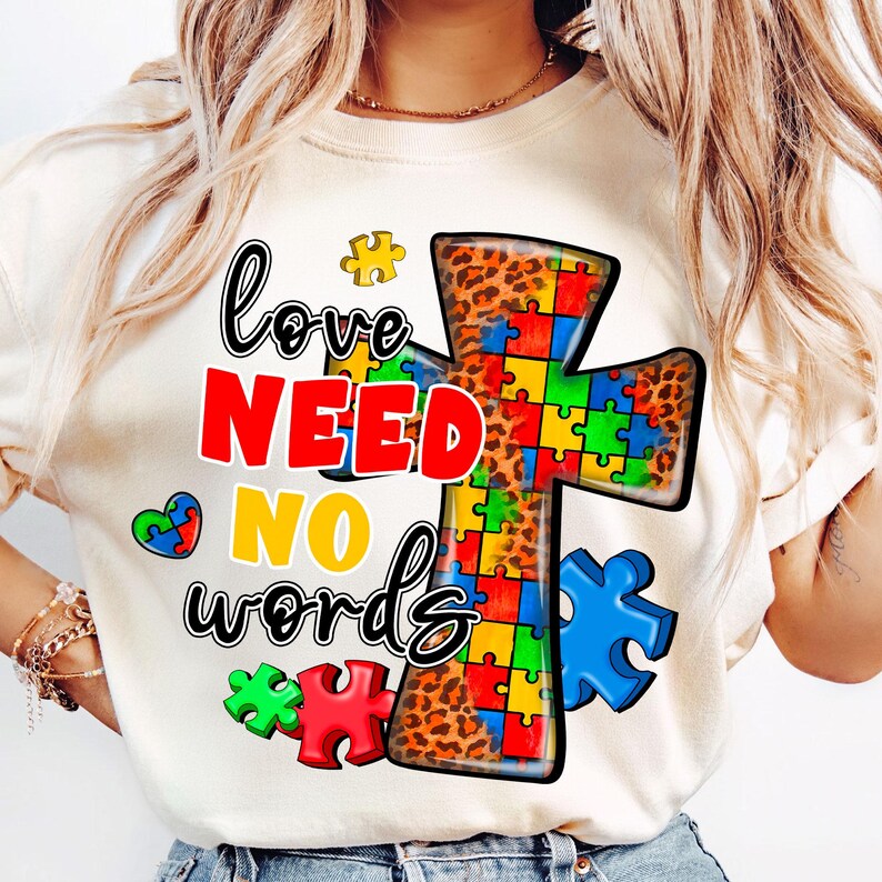 Pu&ograve; includere: Maglietta bianca con un design a croce di pezzi di puzzle colorati e il testo "love need no words".