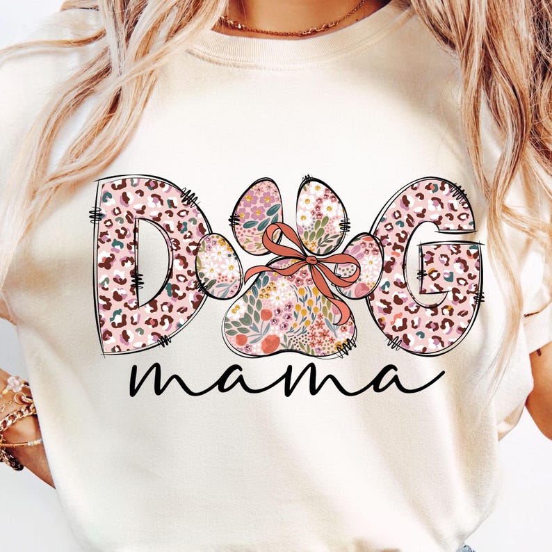 May include: A white t-shirt featuring a pink and brown floral design that reads "Dog mama" with a paw print in the centre.