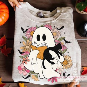 Könnte beinhalten: Hellbeige Sweatshirt mit einem Geist, der ein Buch liest, einer schwarzen Katze, Blumen, Fledermäusen und Sternen. Das Design ist ideal für Halloween oder den Herbst. Der Text "RETROSUBLIMATION DIGITAL DESIGN" befindet sich unten.