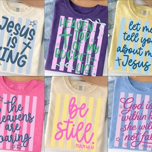 May include: A collection of six t-shirts in various colors, each featuring a unique religious-themed design. The shirts display phrases like "Jesus is King" and "Heaven Top of My Bucket List" in bold, colorful fonts with striped backgrounds.