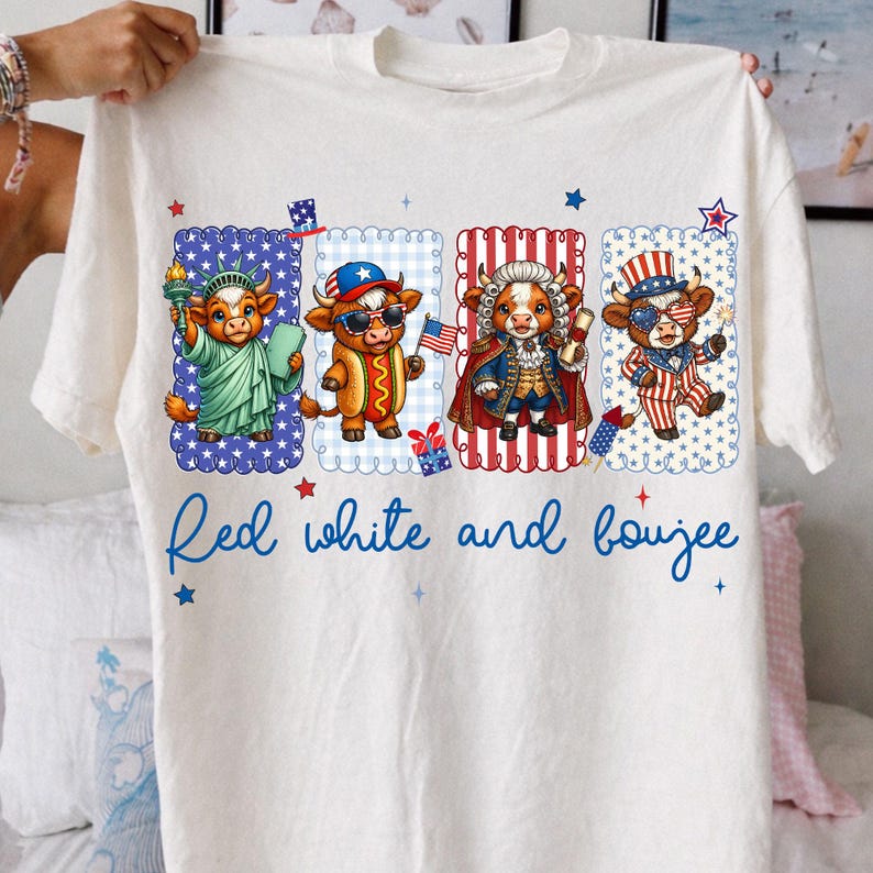 May include: White t-shirt featuring four cartoon cows dressed in patriotic attire. The cows are depicted as the Statue of Liberty, a hot dog, a historical figure, and a Fourth of July celebrant. The text "Red white and boujee" is written in blue script.