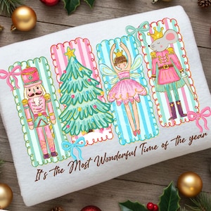 May include: White towel with a festive design featuring a nutcracker, Christmas tree, fairy, and mouse in pink, green, and blue. The text "It's the Most Wonderful Time of the year" is printed at the bottom. Decorative bows and gold baubles surround the towel.