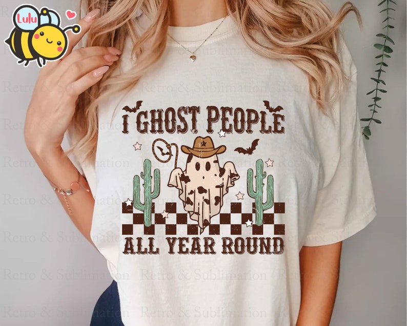 May include: A white t-shirt featuring a graphic of a ghost wearing a cowboy hat and the text "I ghost people all year round". The ghost is surrounded by cacti and stars.