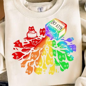 Könnte beinhalten: Ein weißes Sweatshirt mit einem Regenbogenmuster aus Katzen, die aus einer Flasche mit der Aufschrift "Ally Cat" fließen.