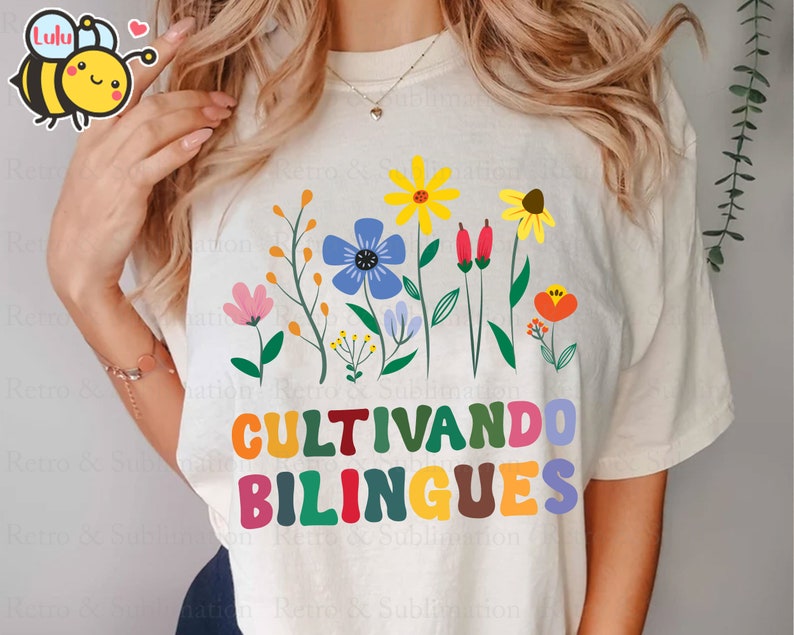 Peut inclure: Un t-shirt blanc avec un motif floral color&eacute; et le texte "Cultivando bilingues" en lettres arc-en-ciel.