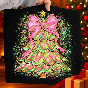 Puede incluir: Bolso tote negro con un diseño de árbol de Navidad colorido. El árbol está adornado con un lazo rosa y una estrella dorada, con una vibrante mezcla de colores y detalles de estrellas. El diseño está sobre un fondo negro.
