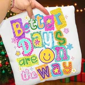 May include: White pillow with the phrase "Better Days are on the Way" in colorful, cut-out style letters. The design includes a yellow smiley face, stars, and floral accents, creating a cheerful and optimistic aesthetic.