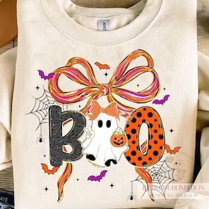 May include: Cream-colored sweatshirt with a Halloween-themed graphic. The word "BOO" is spelled out with a black leopard print "B", a ghost, and an orange polka-dot "O". A large bow and bats complete the design.