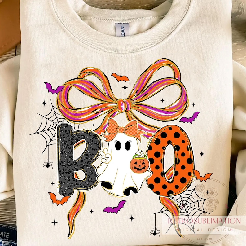 May include: Cream-colored sweatshirt with a Halloween-themed graphic. The word "BOO" is spelled out with a black leopard print "B", a ghost, and an orange polka-dot "O". A large bow and bats complete the design.