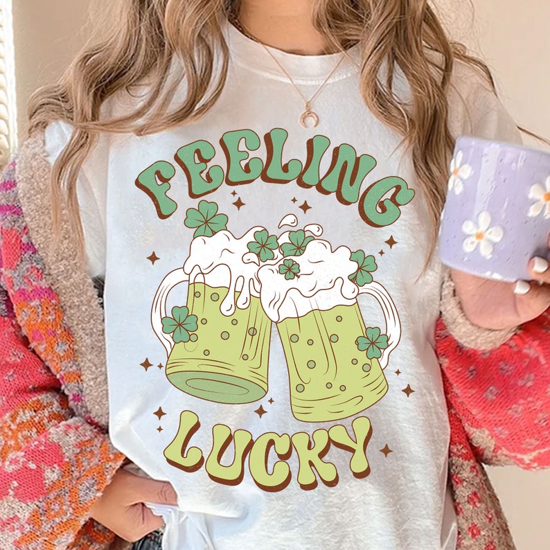 May include: White t-shirt with a green and white graphic of two beer mugs with shamrocks and the text "Feeling Lucky".