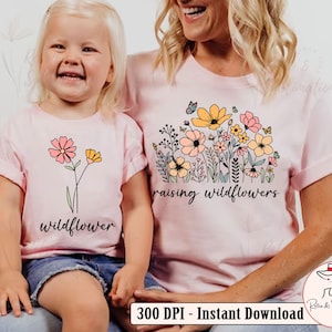 May include: Two pink t-shirts with a floral design and the text "raising wildflowers" and "wildflower".