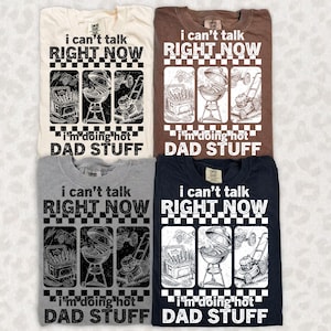 May include: Four t-shirts in cream, brown, gray, and navy blue, each with a graphic design. The design includes the text "I can't talk RIGHT NOW" above three illustrations of grilling and yard work, and the text "I'm doing hot DAD STUFF" below.