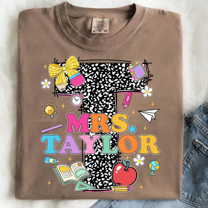 May include: A brown t-shirt featuring a colorful design for a teacher. The design includes the text "MRS. TAYLOR" in vibrant, retro-style lettering, surrounded by school-themed illustrations like an apple, pencil, and notebook paper.