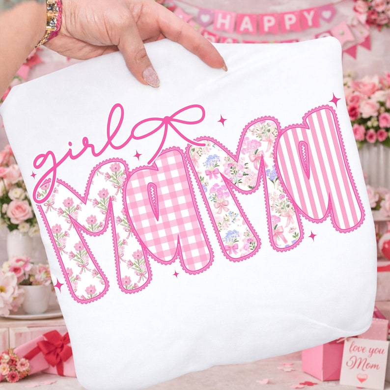 Puede incluir: Coj&iacute;n blanco con las palabras "girl mama" en rosa. Las letras est&aacute;n decoradas con estampados florales, cuadros vichy y rayas. Un lazo rosa est&aacute; encima de la palabra "girl".