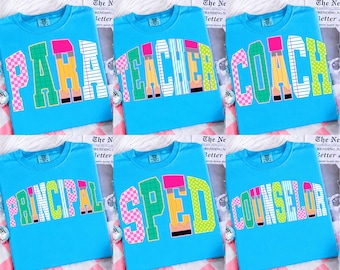 Könnte beinhalten: Sechs hellblaue T-Shirts mit verschiedenen Wörtern in einer Schriftart im College-Stil. Die Wörter lauten "PARA", "TEACHER", "COACH", "PRINCIPAL", "SPED" und "COUNSELOR". Die Buchstaben sind in verschiedenen Farben und Mustern, darunter Rosa, Grün und Gelb.