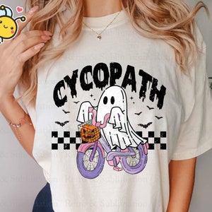 May include: White t-shirt with a black and white graphic of a ghost riding a bicycle with a pumpkin in the basket. The text "CYCOPATH" is above the ghost.