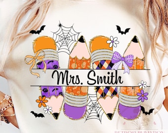 May include: A cream-coloured t-shirt with a Halloween-themed pencil design and the name "Mrs. Smith". The pencils are decorated with orange, purple, and black patterns, spiderwebs, bats, and bows. Small flowers are also included in the design.