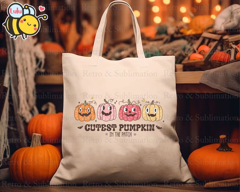 Może przedstawiać: Biała torba z pł&oacute;tna z nadrukiem trzech dyń z twarzami. Dynie są pomarańczowe, r&oacute;żowe i ż&oacute;łte. Tekst na torbie brzmi "Cutest Pumpkin in the Patch".