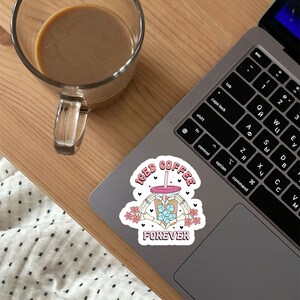 Puede incluir: Una pegatina blanca con un vaso de caf&eacute; helado de dibujos animados rosa y azul con una pajita y cubitos de hielo. El vaso est&aacute; sostenido por dos manos esquel&eacute;ticas. El texto "ICED COFFEE FOREVER" est&aacute; escrito en letras rosas alrededor del vaso.