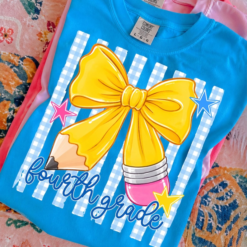 Może przedstawiać: Jasnoniebieski t-shirt z grafiką przedstawiającą dużą ż&oacute;łtą kokardę połączoną z oł&oacute;wkiem. Nadruk zawiera biało-niebieskie paski w kratkę vichy, r&oacute;żową gumkę do mazania oraz niebieski napis fourth grade ozdobiony małymi gwiazdkami.
