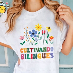Peut inclure: T-shirt blanc avec un motif graphique color&eacute; repr&eacute;sentant des fleurs et le texte "CULTIVANDO BILINGUES".