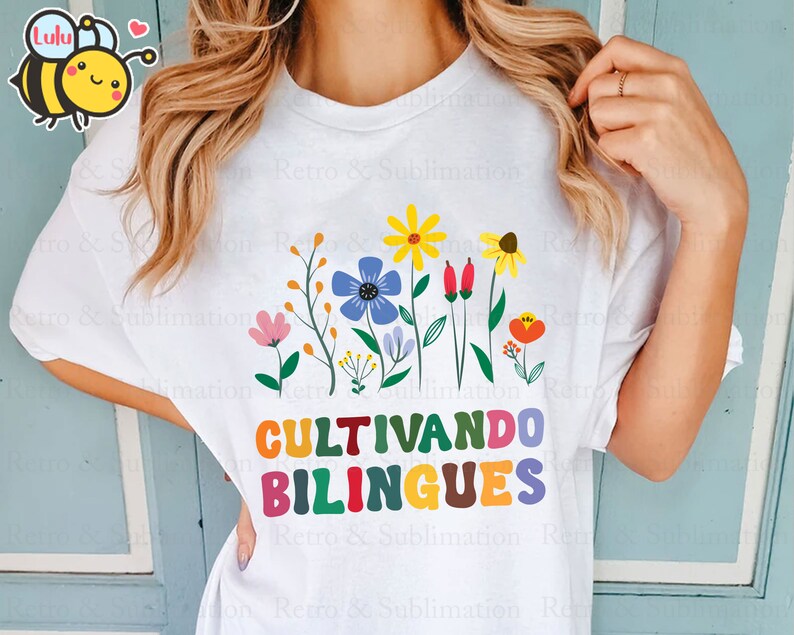 Peut inclure: T-shirt blanc avec un motif graphique color&eacute; repr&eacute;sentant des fleurs et le texte "CULTIVANDO BILINGUES".