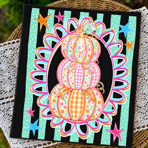 May include: A rectangular fabric panel featuring a stack of three pumpkins with floral and gingham patterns in orange, pink, and blue. The pumpkins are centered within a vibrant, multi-colored ribbon frame against a black and teal striped background.