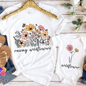 May include: Two white t-shirts with a floral design and the text "raising wildflowers" and "wildflower".