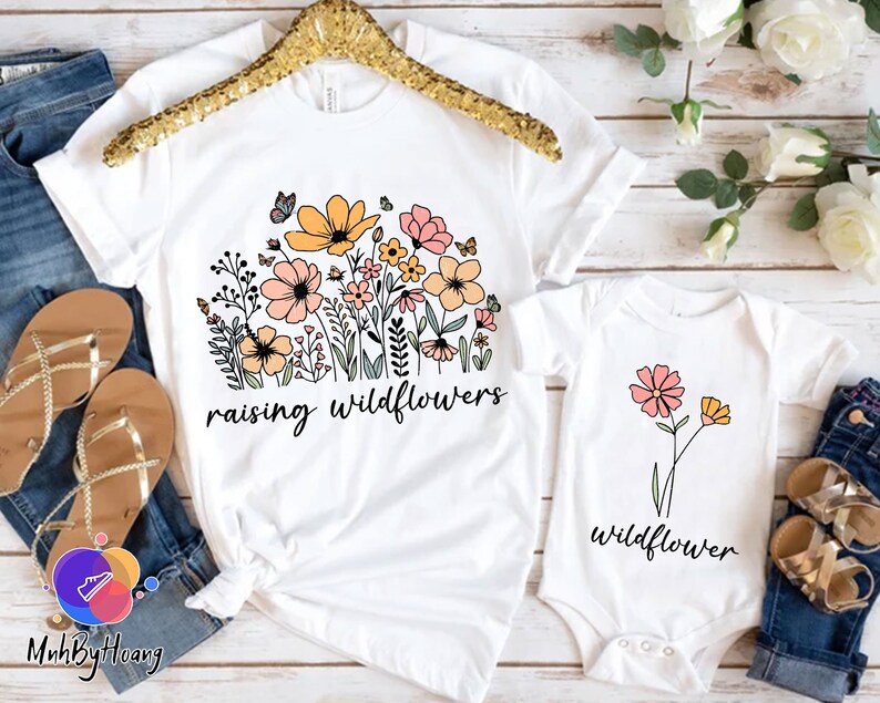 May include: Two white t-shirts with a floral design and the text "raising wildflowers" and "wildflower".