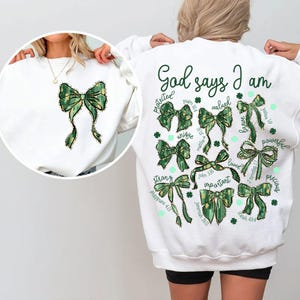 May include: White sweatshirt with a green and gold bow design and the text "God says I am" with a list of positive affirmations and bible verses.