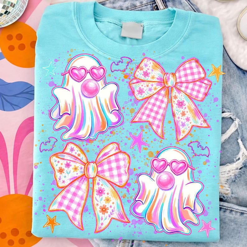 May include: A light blue t-shirt featuring a graphic print of two white ghosts wearing pink heart-shaped sunglasses and blowing pink bubblegum bubbles, accompanied by two large pink and white checkered bows with floral patterns and small stars.