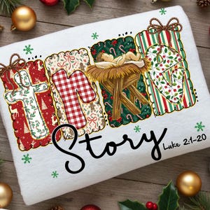 Op de afbeelding: Witte kersthanddoek met de woorden "NATIVITY STORY" in een decoratief lettertype. De letters zijn gevuld met feestelijke patronen, waaronder een kruis, ruitjes en een kerststal. De tekst "Lucas 2:1-20" is ook aanwezig.