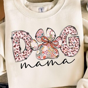 May include: A cream-coloured sweatshirt with a pink and brown floral design that says "Dog mama".